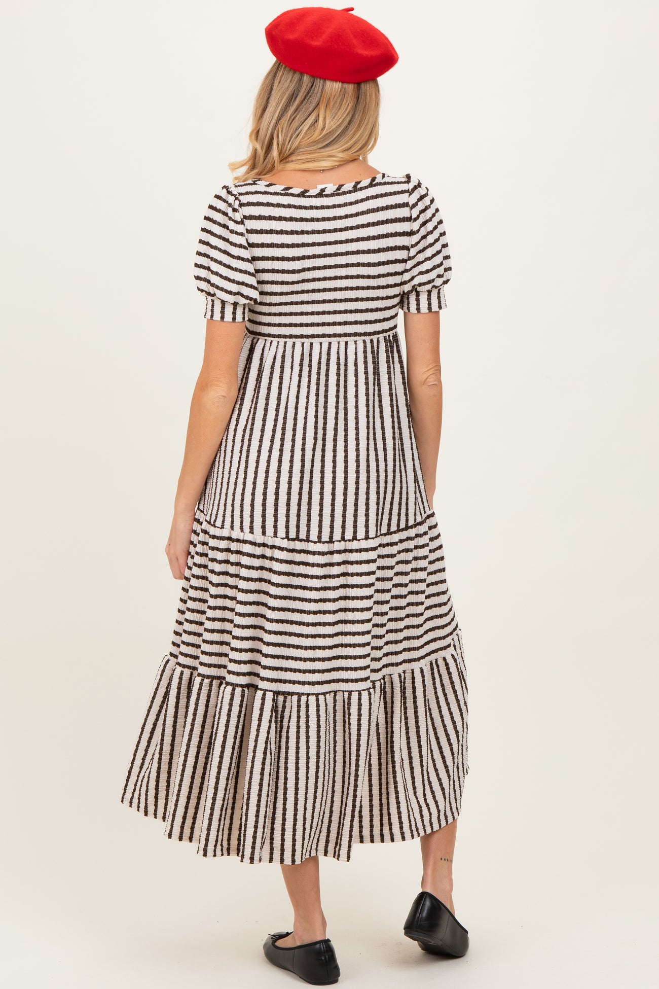 woman wearing a striped maternity maxi dress with short puff sleeves and a tiered skirt, showing her baby bump