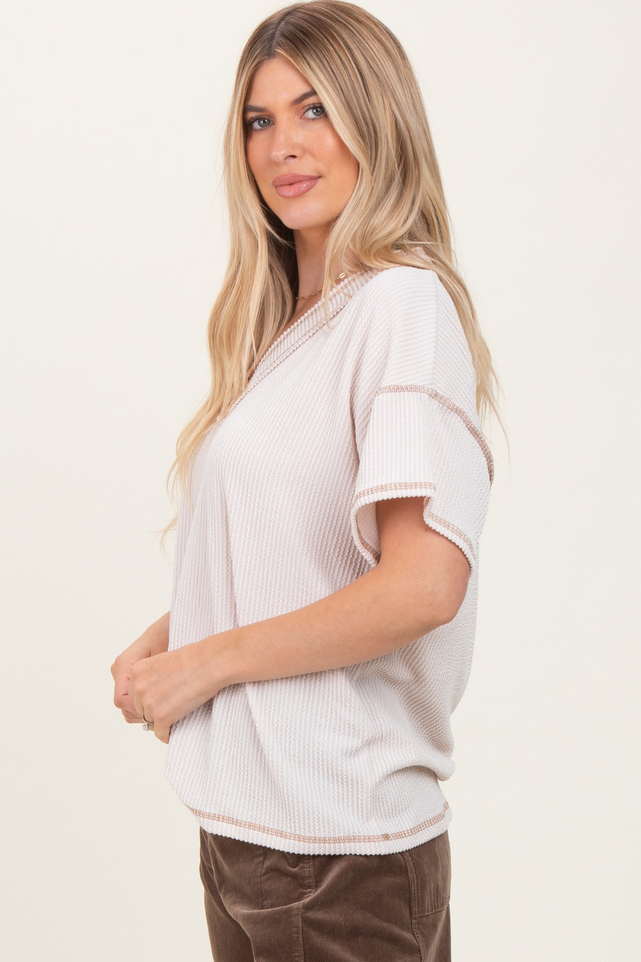 woman wearing a beige short sleeve top with ribbed texture and contrasting trim, styled with brown corduroy pants