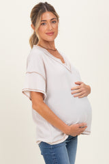 woman wearing a light taupe maternity top with a v-neck and holding her baby bump