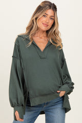 woman wearing a dark green maternity pullover with a v-neck and loose sleeves, styled with casual blue jeans