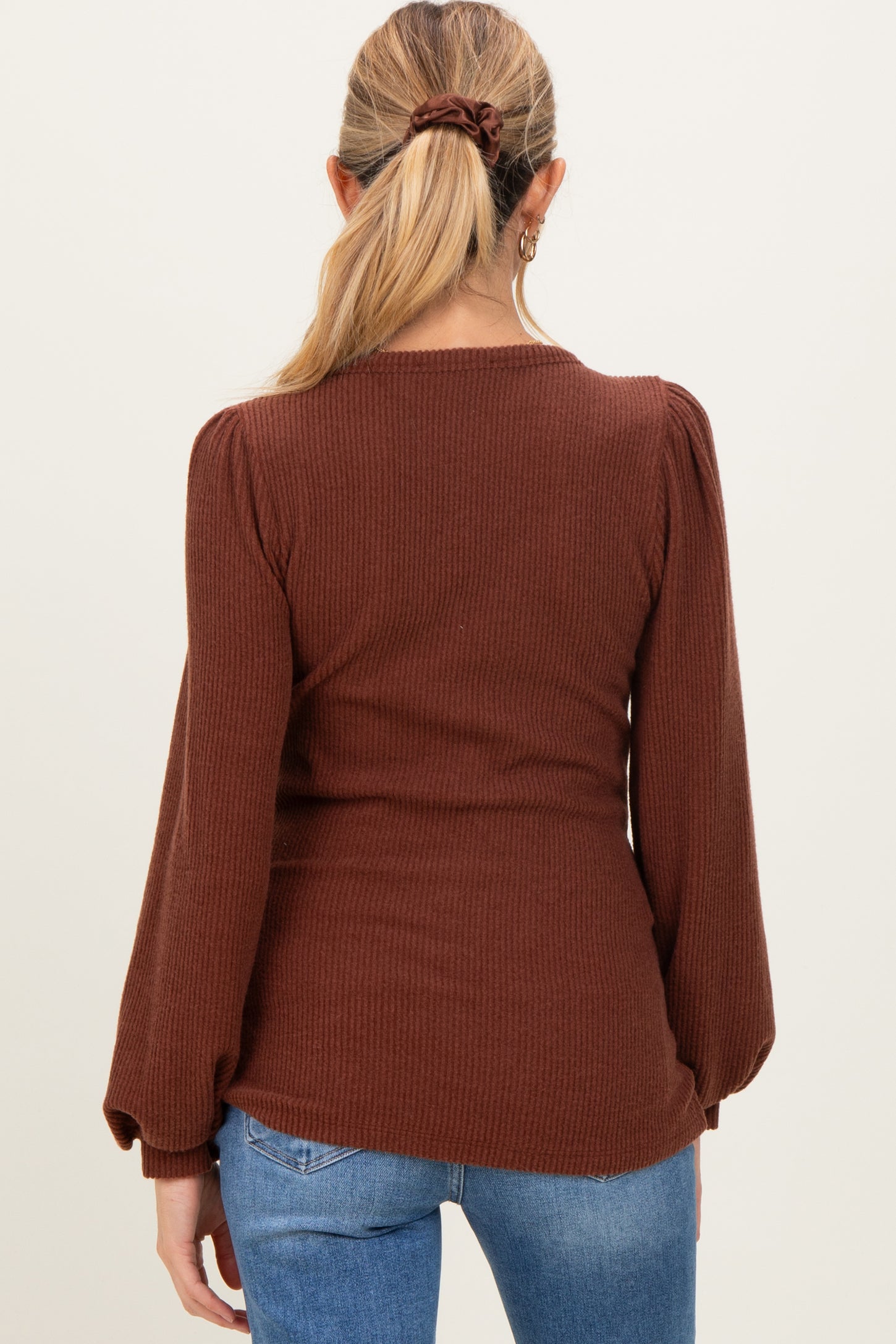 woman wearing a brown ribbed maternity top with puffed sleeves, showing her back against a neutral background