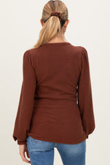 woman wearing a brown ribbed maternity top with puffed sleeves, showing her back against a neutral background