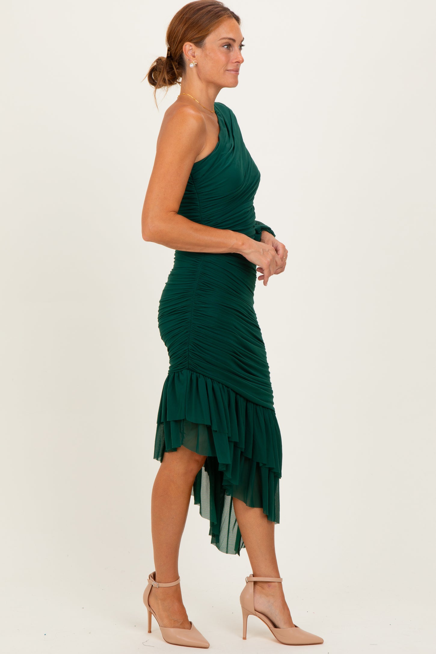 woman wearing a green one-shoulder ruched dress with a high-low hem and ruffle details