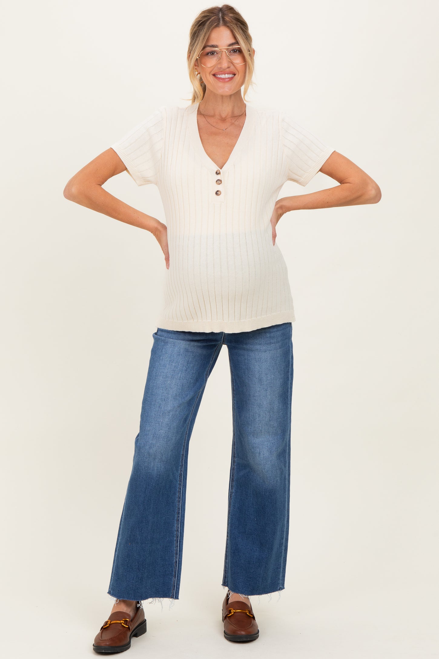 woman wearing a cream maternity top with ribbed texture and buttons, paired with blue flared jeans and showing her baby bump