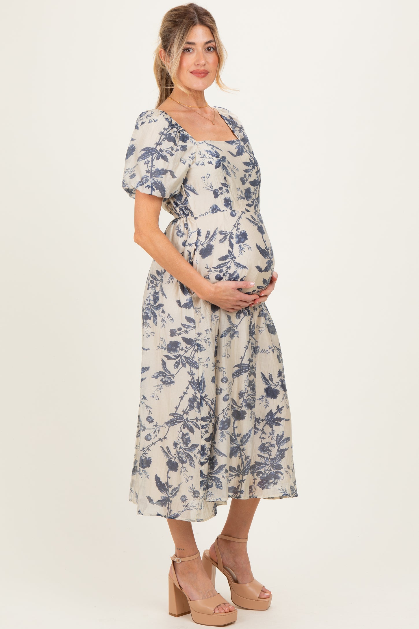 woman wearing a floral print maternity dress with puff sleeves and holding her baby bump