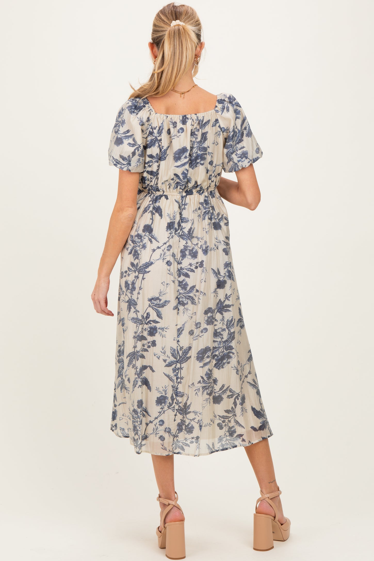 woman wearing a floral print cream maternity dress with a gathered waist and short puff sleeves