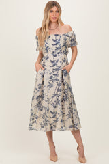 woman wearing a floral off-the-shoulder midi dress with pockets and a light beige background