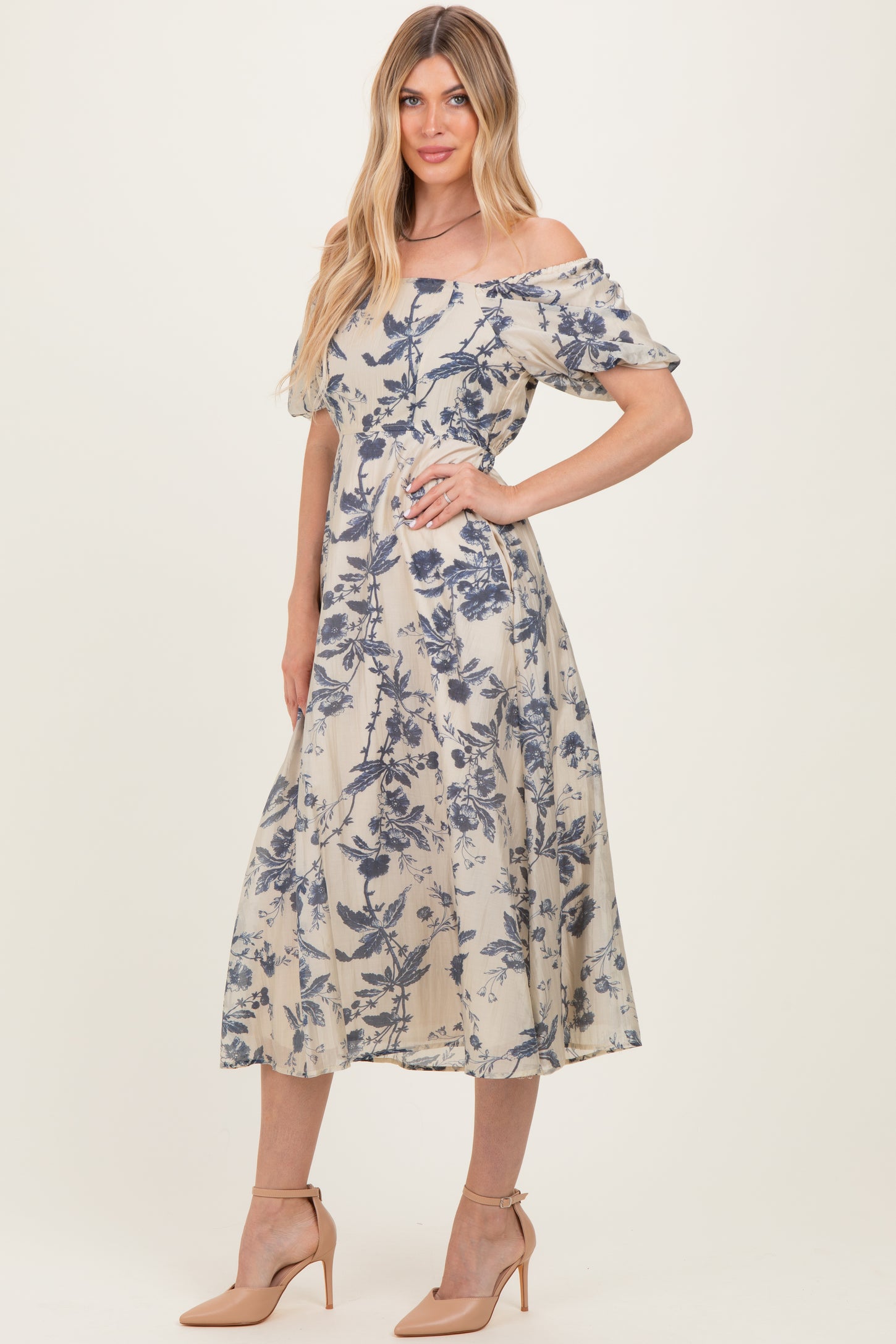 woman wearing a floral off-the-shoulder midi dress in beige and blue with short puff sleeves and a fitted waist