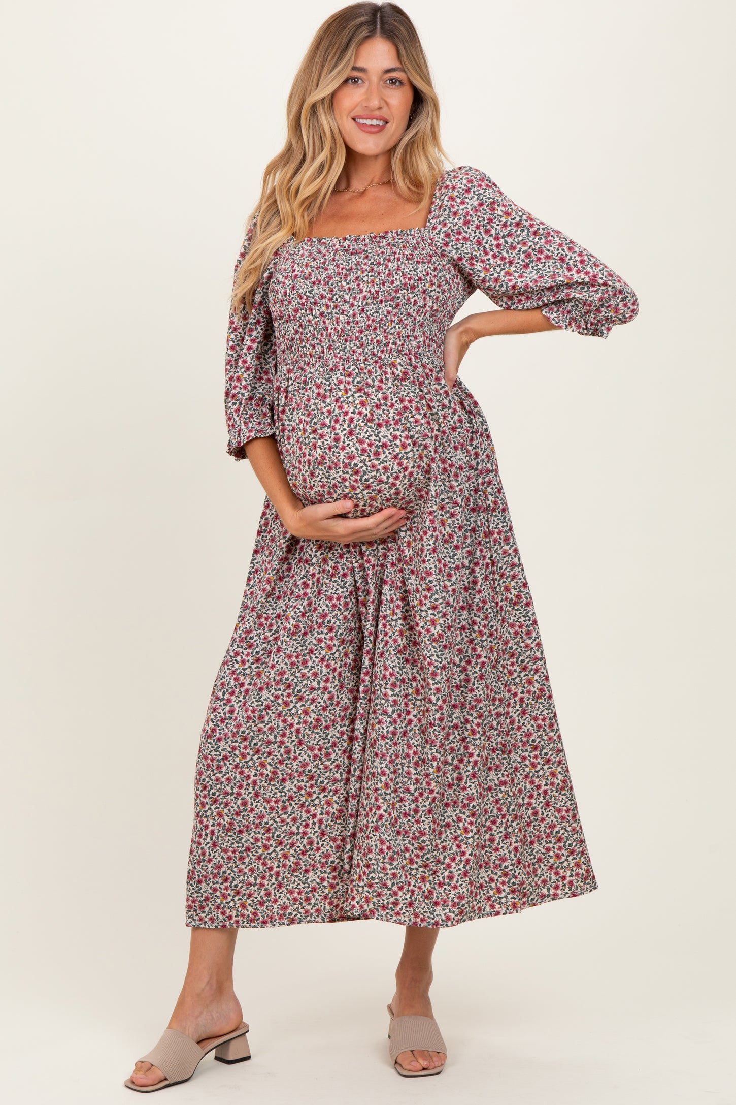 woman wearing a floral print maternity maxi dress with a square neckline and puff sleeves, holding her baby bump