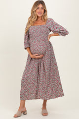 woman wearing a floral print maternity maxi dress with a square neckline and puff sleeves, holding her baby bump