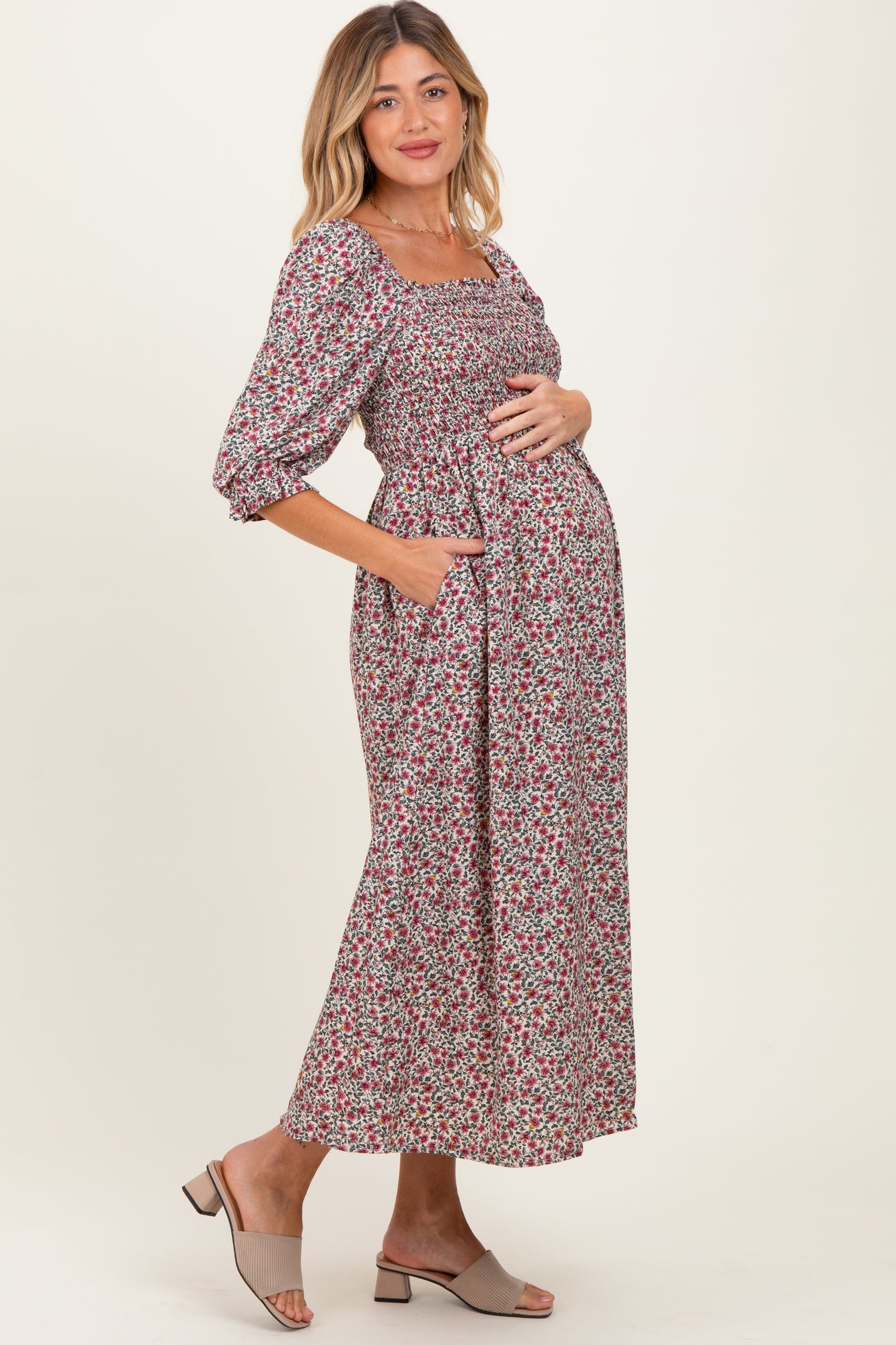woman wearing a floral maternity midi dress with puff sleeves and a pocket, cradling her baby bump