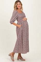 woman wearing a floral maternity midi dress with puff sleeves and a pocket, cradling her baby bump