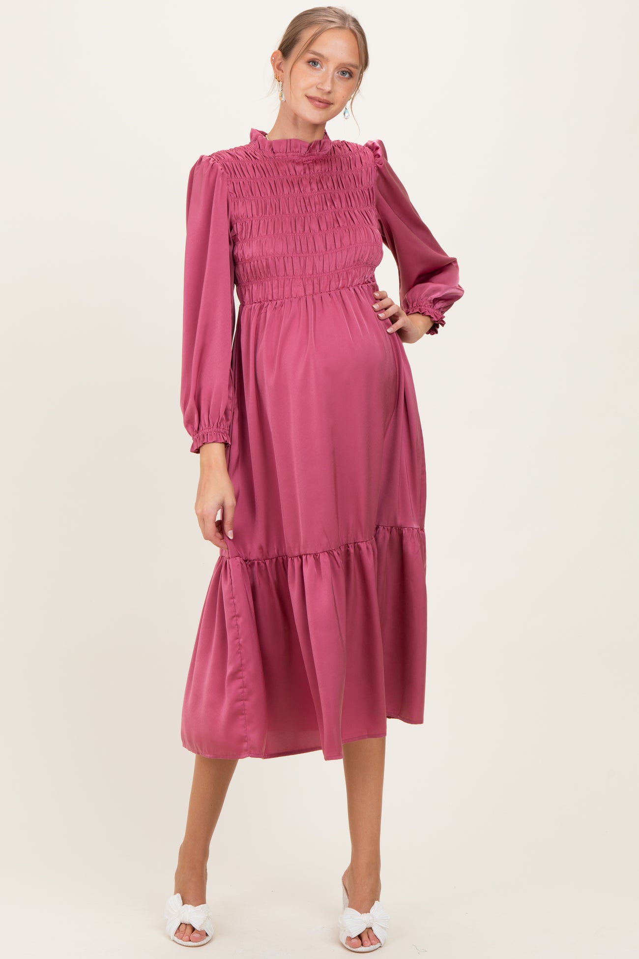 woman wearing a pink smocked maternity dress with long sleeves and a flowy skirt, showing her baby bump
