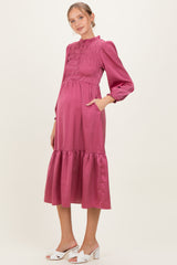 woman wearing a magenta maternity dress with smocking details and long sleeves, showing her baby bump