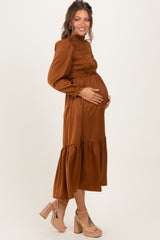 woman wearing a rust-colored maternity dress with smocked bodice and tiered skirt, gently cradling her baby bump