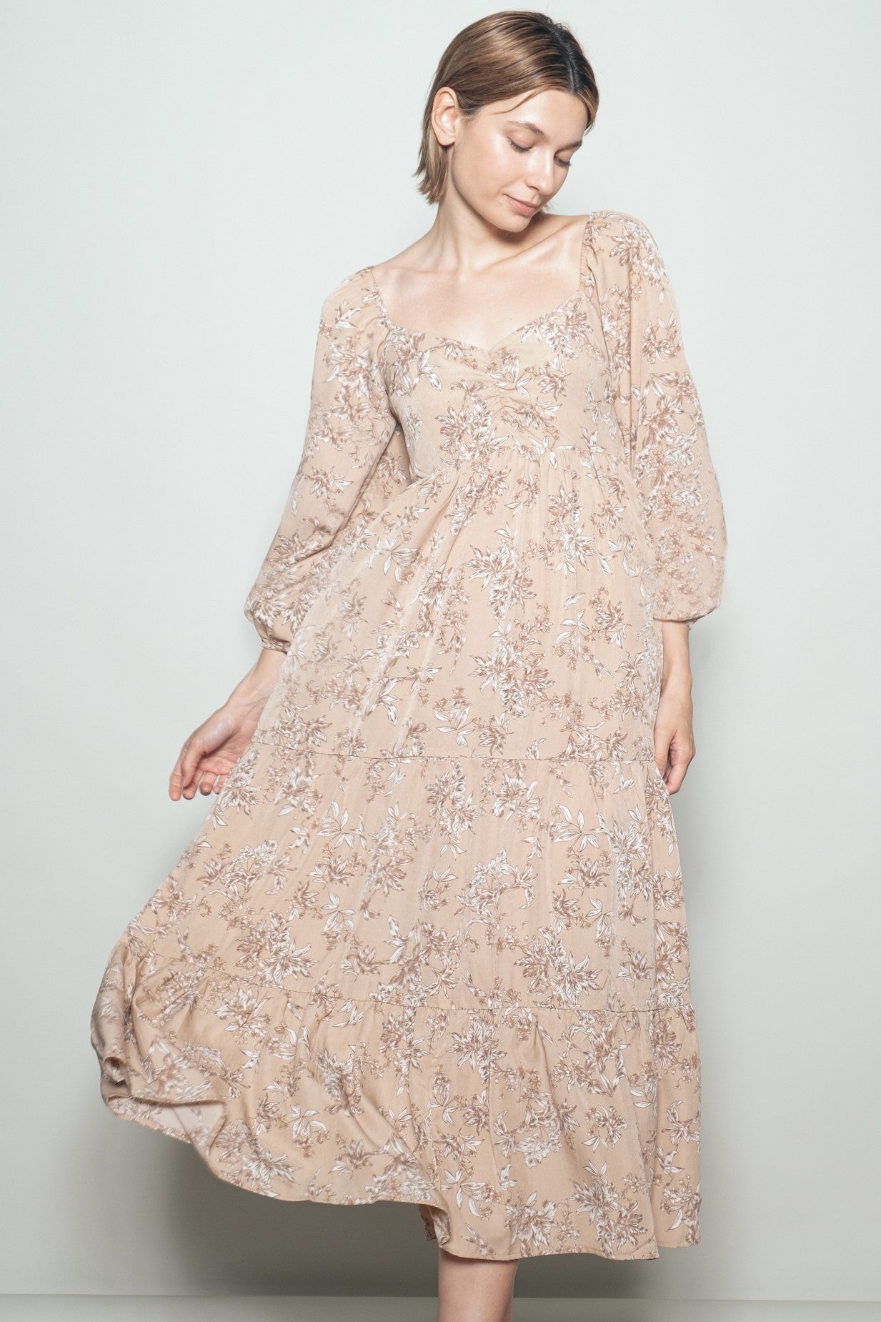 woman wearing a beige floral midi dress with puff sleeves, twirling slightly against a light background