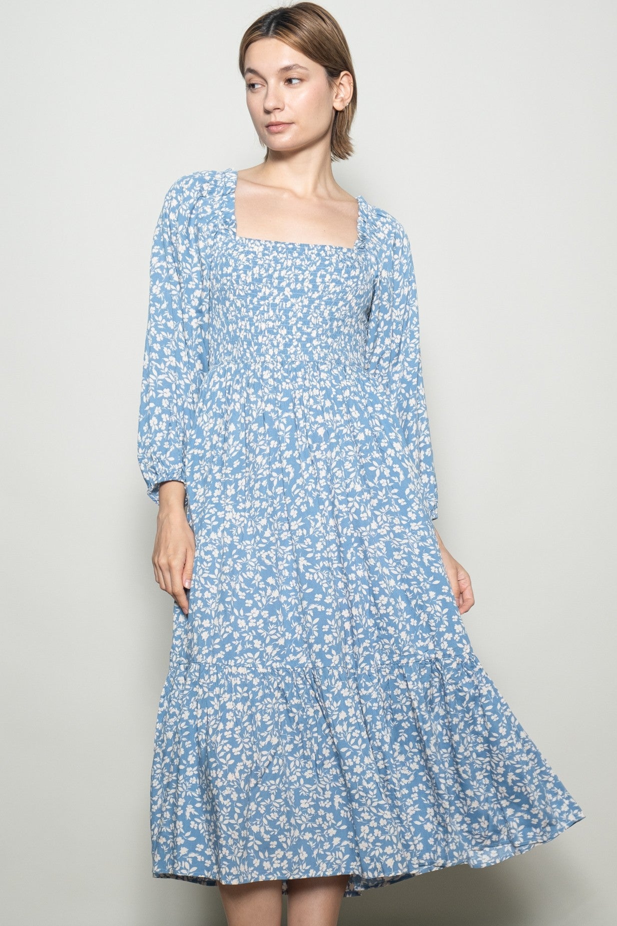 woman wearing a light blue floral long sleeve midi dress with a square neckline and tiered skirt