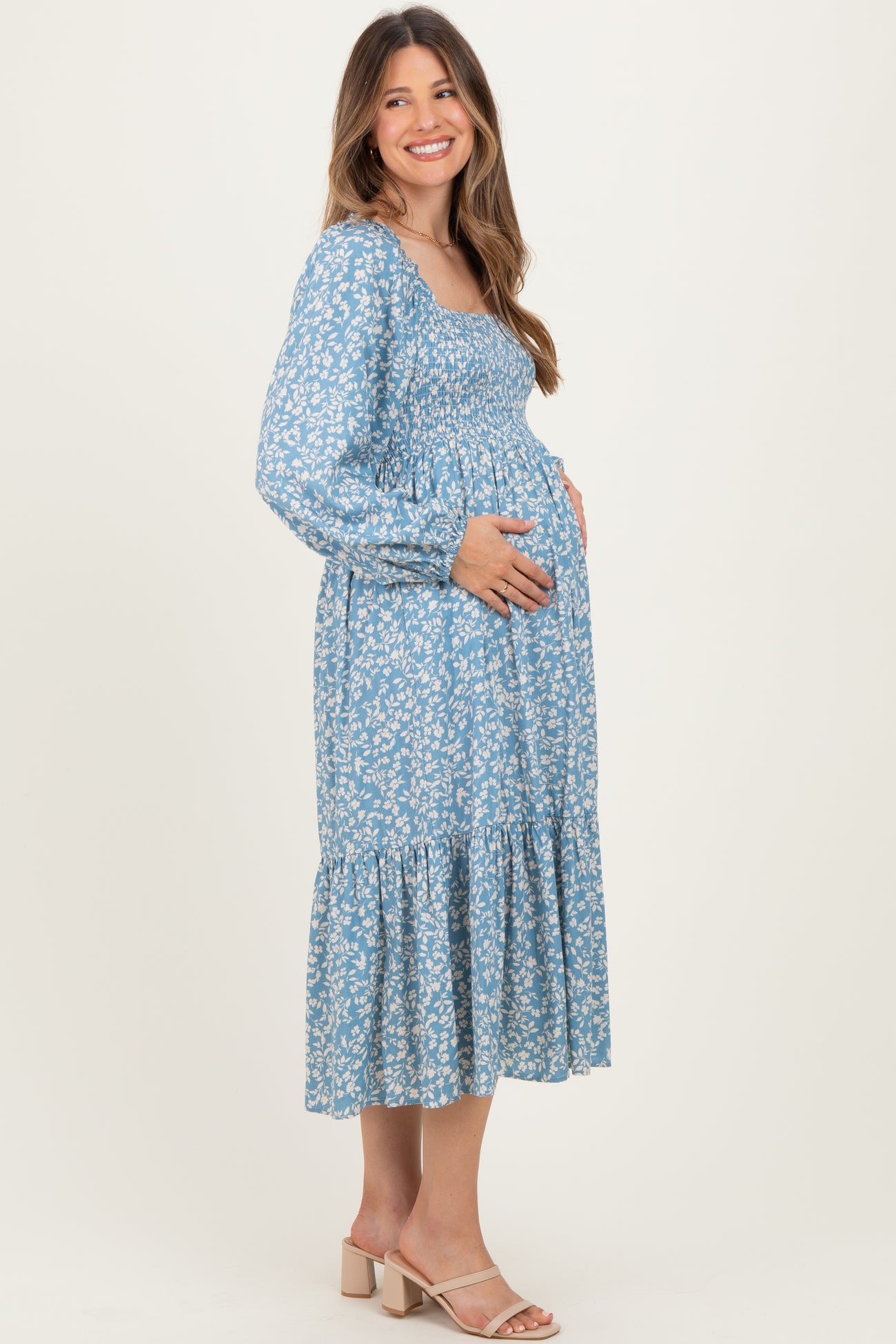 woman wearing a light blue floral maternity dress with long sleeves and a tiered hem, holding her baby bump