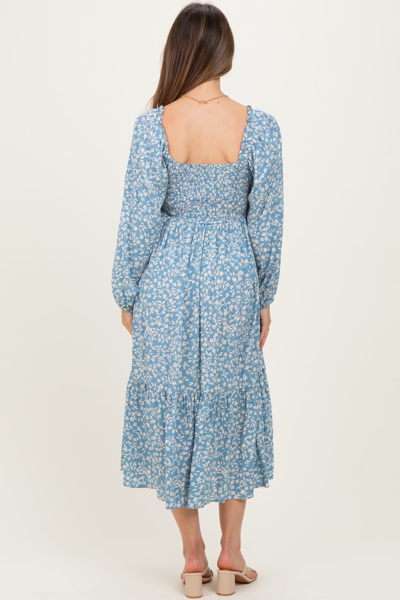 woman wearing a blue floral maternity dress with a square neckline and long sleeves, showing a back view