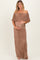 woman wearing a brown off-shoulder maternity dress with ruffle detailing and holding her baby bump
