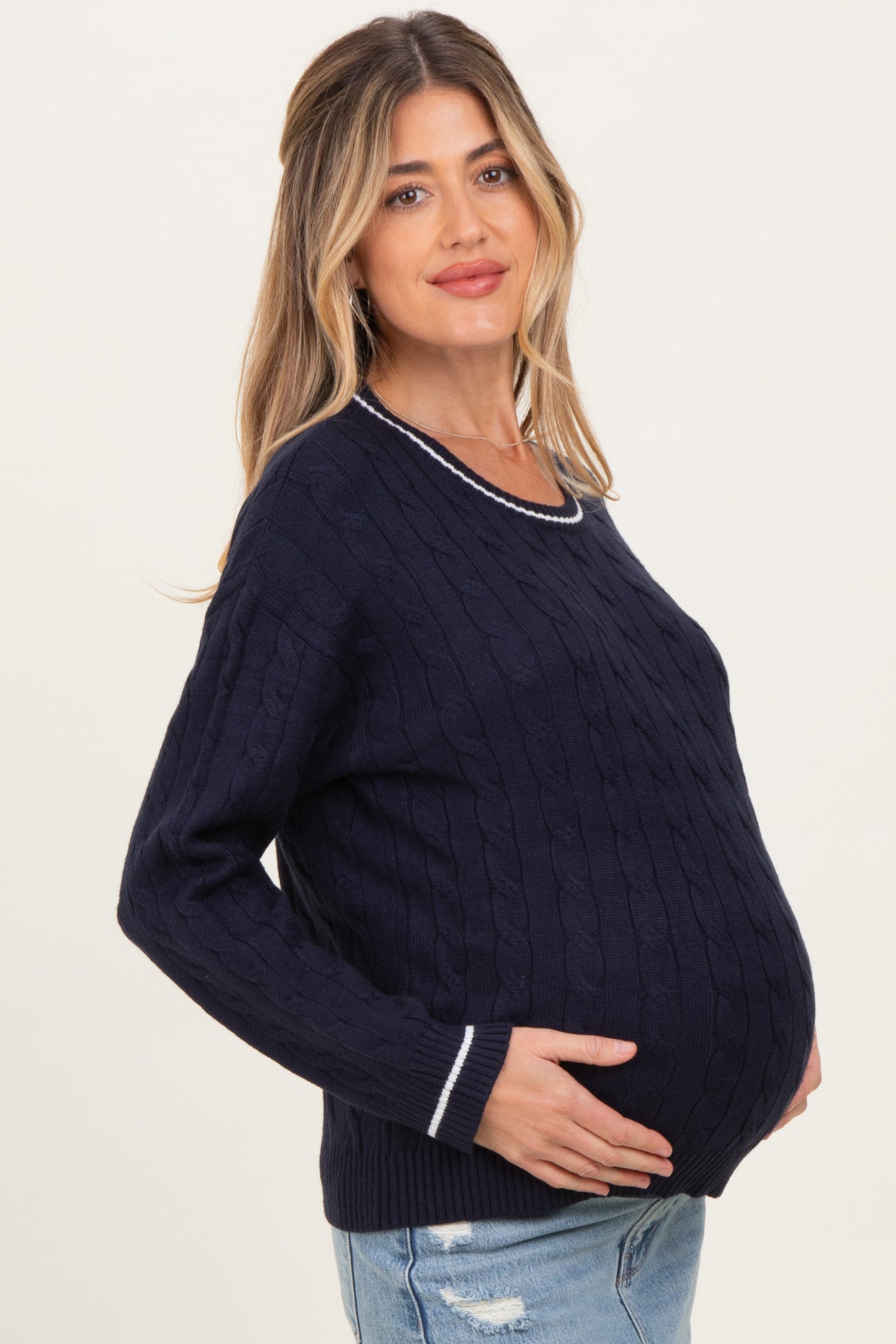 woman wearing a navy blue cable knit maternity sweater with white trim and holding her baby bump