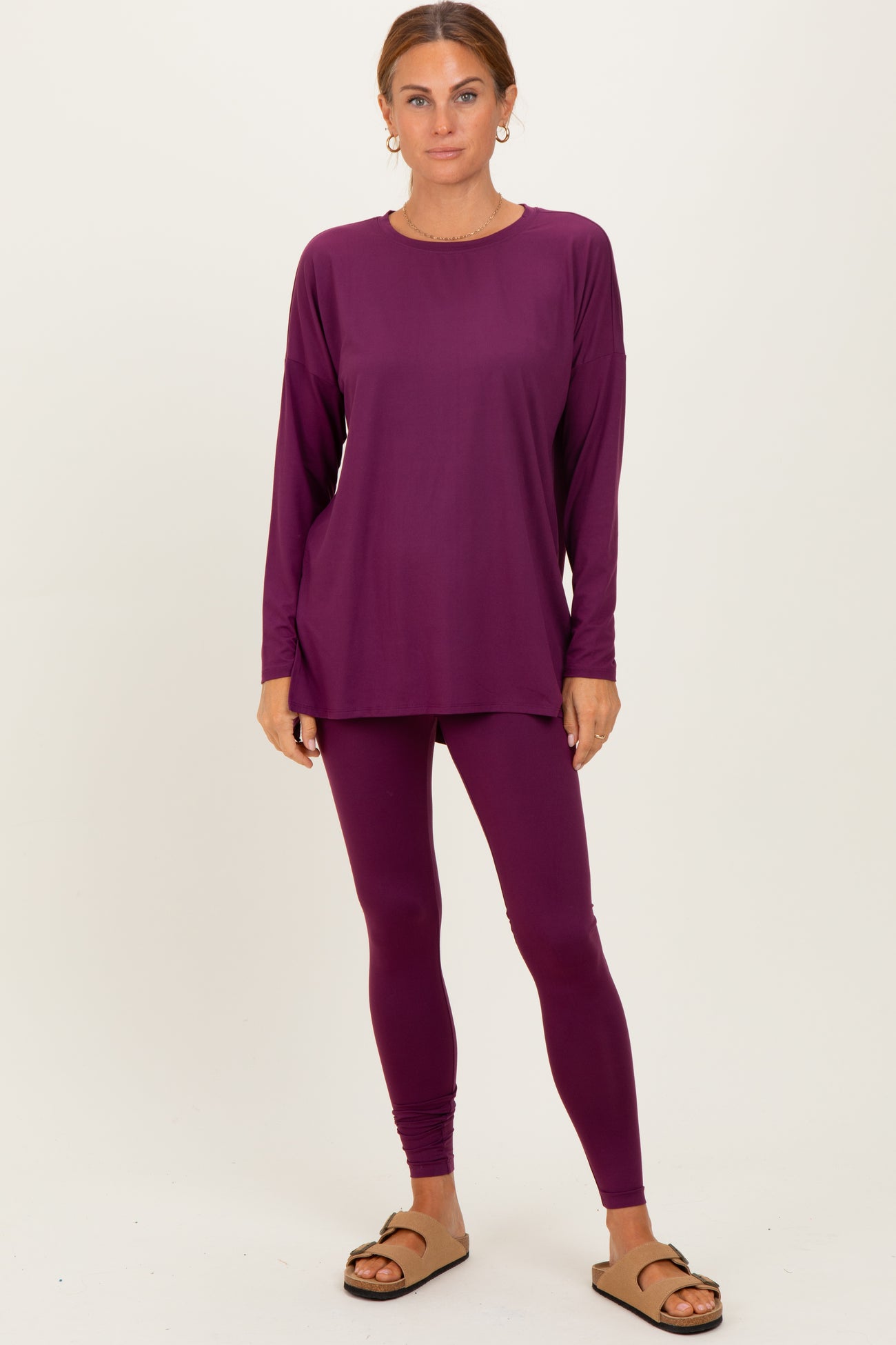 woman wearing a dark purple long sleeve top and matching leggings, standing barefoot