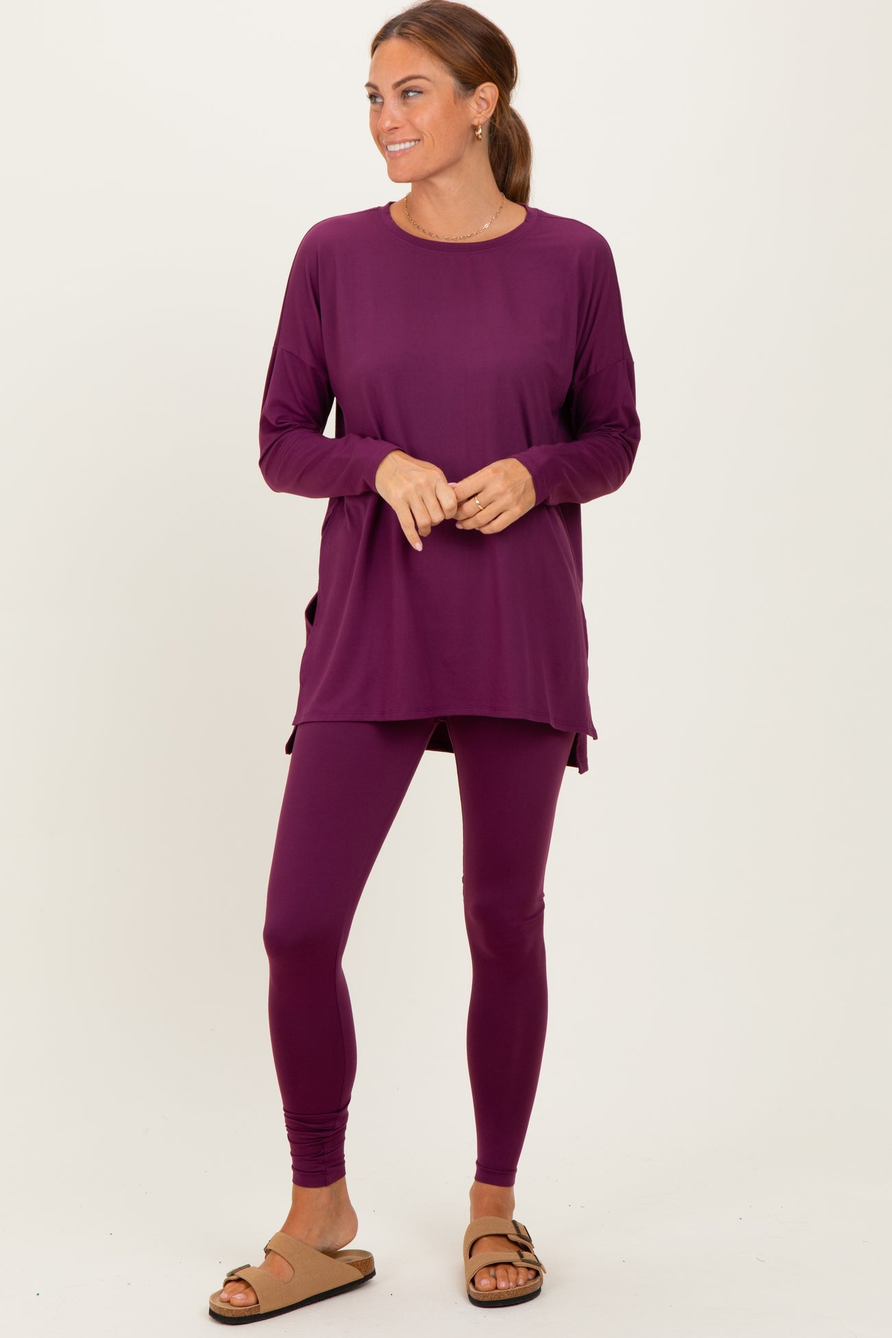 woman wearing a purple long sleeve tunic top with side slits and matching leggings, standing in sandals