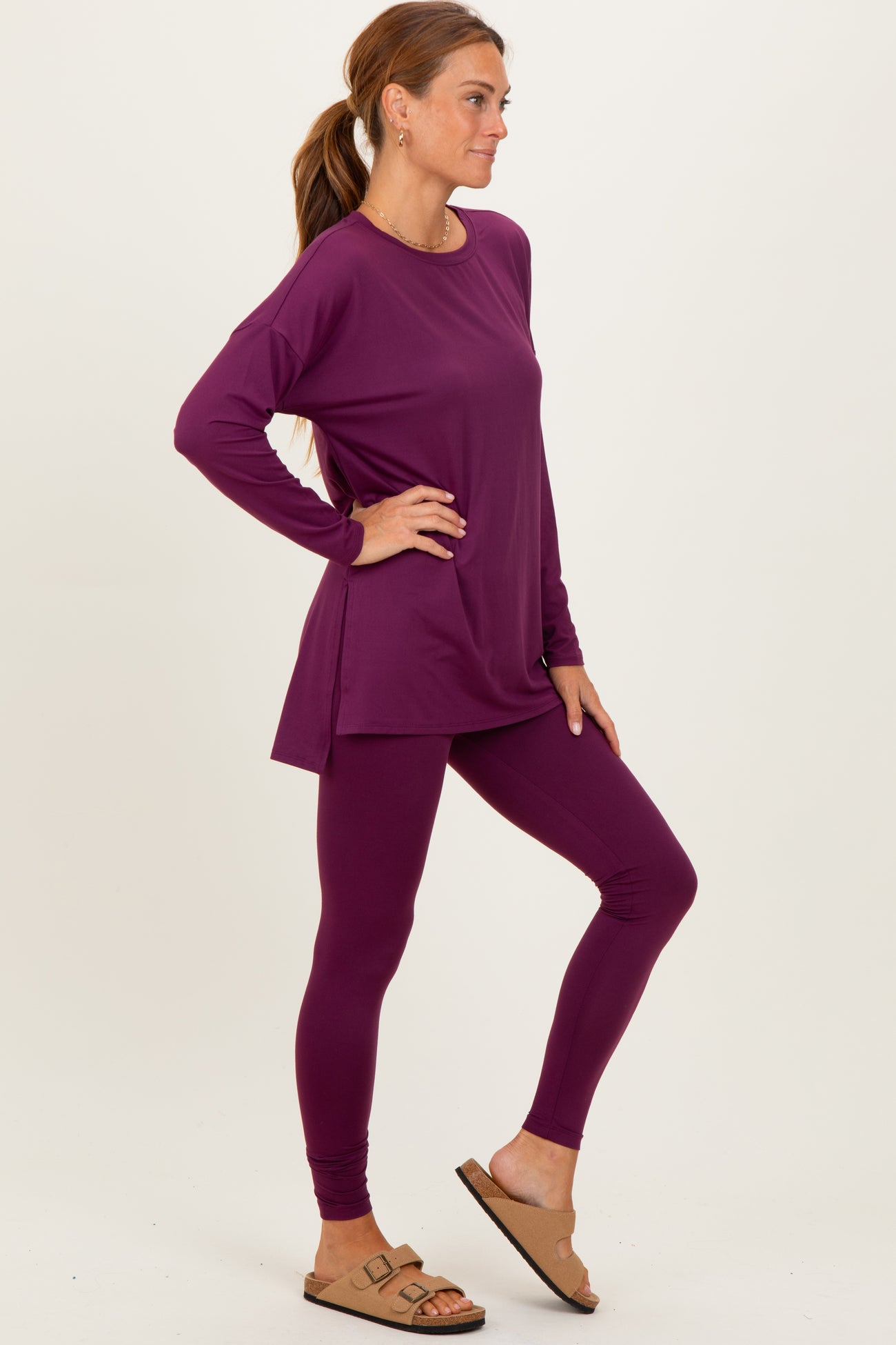 woman wearing a purple long sleeve top and matching leggings, standing with one leg slightly bent