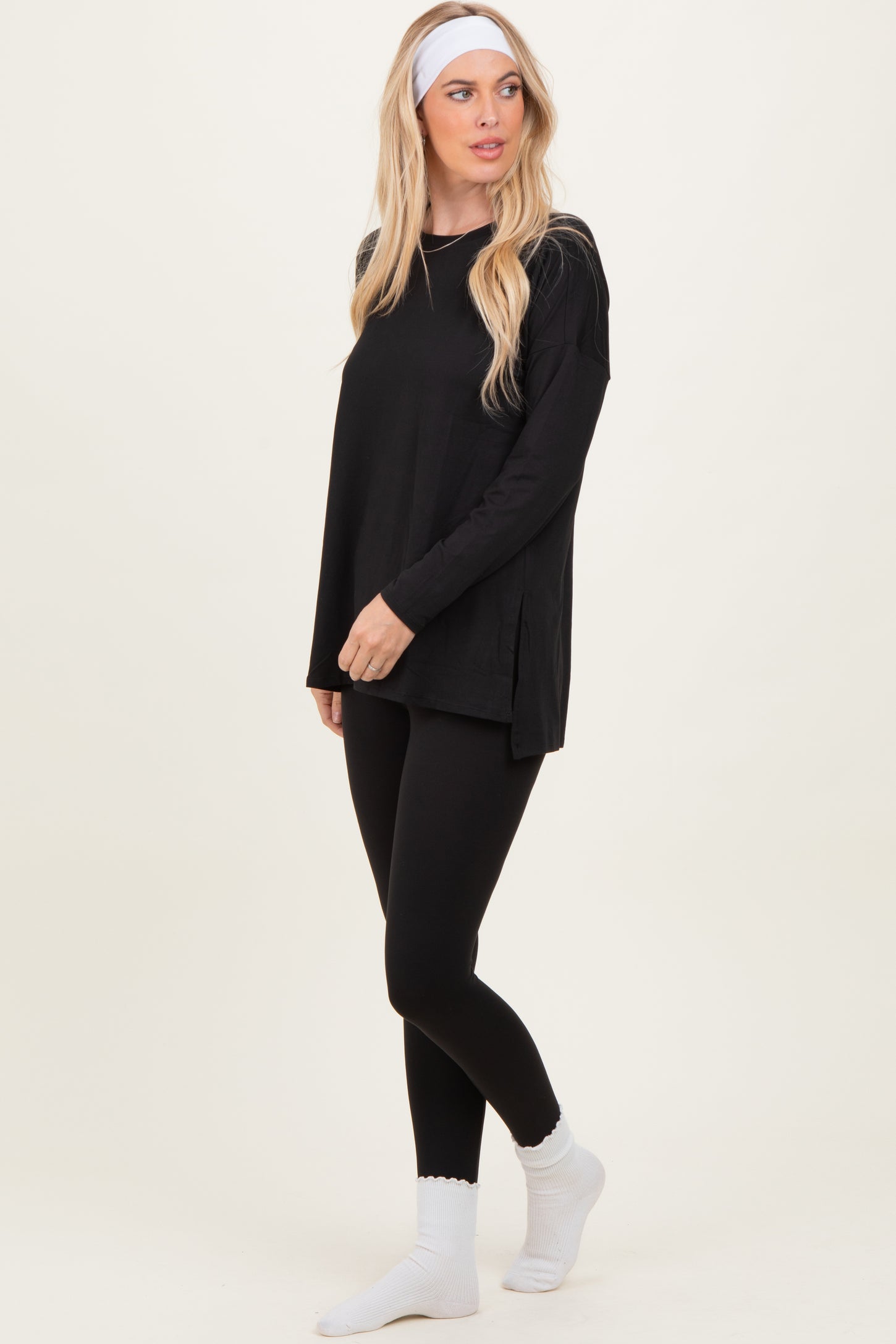 woman wearing a black long sleeve top with side slits and black leggings, styled with a headband and white socks