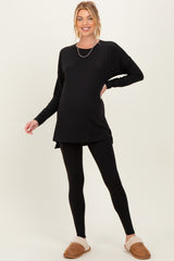 woman wearing a black long sleeve maternity top with leggings and cozy slippers, showing a baby bump
