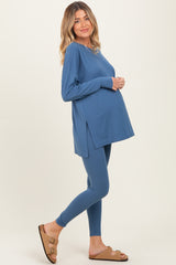 woman wearing a blue long sleeve maternity top and leggings, showcasing her baby bump while smiling at the camera