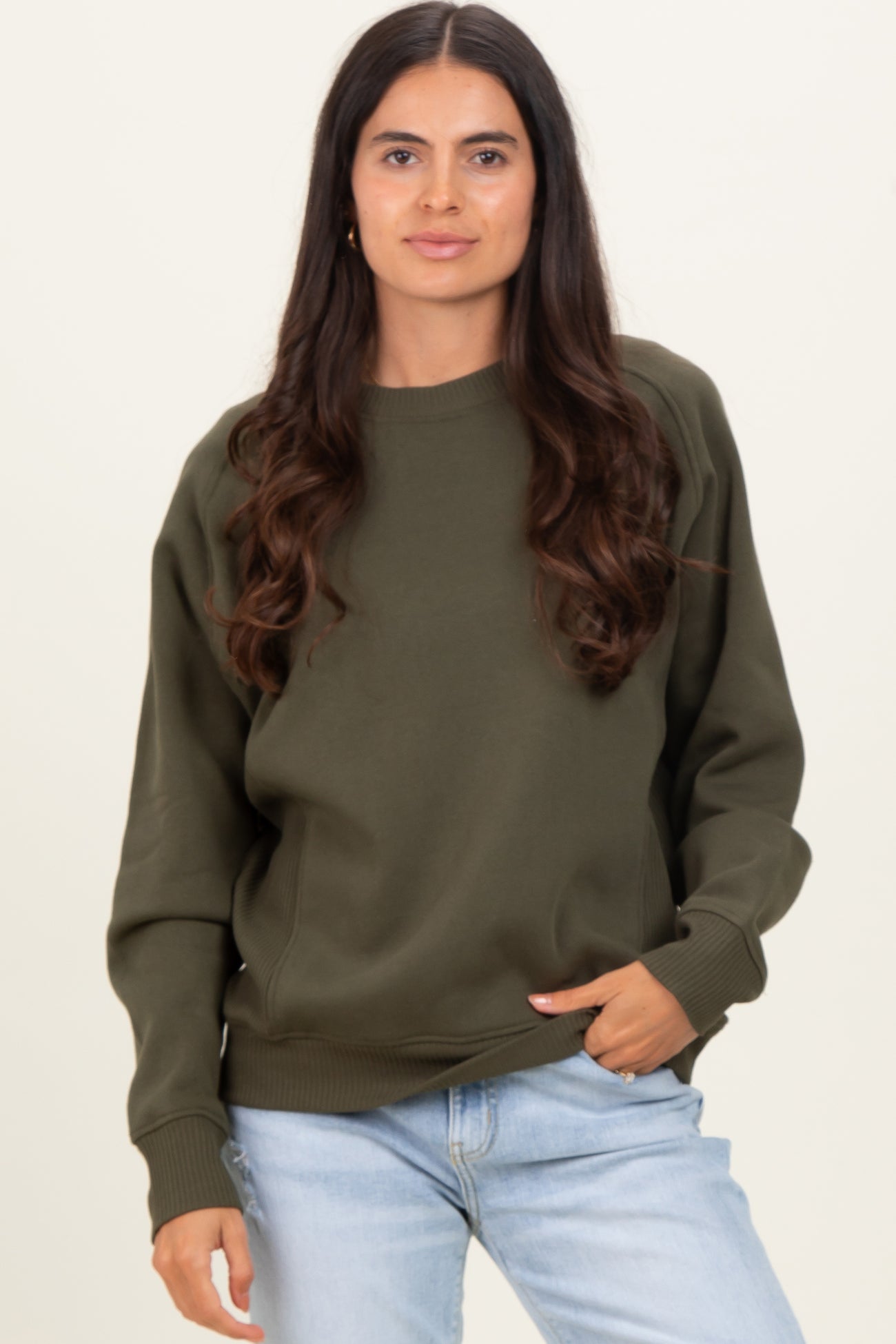 woman wearing an olive green oversized sweatshirt with a round neckline and relaxed fit, paired with light blue jeans