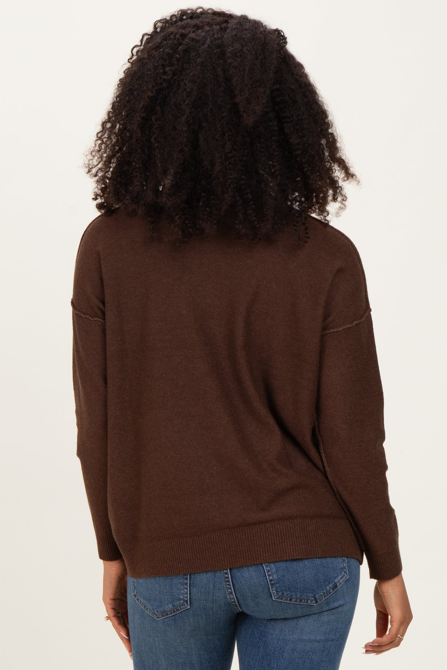 woman wearing a brown oversized sweater with long sleeves and back view, paired with blue jeans