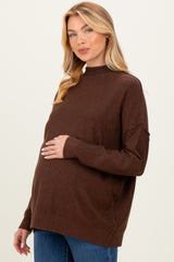 woman wearing a brown maternity sweater with a relaxed fit, gently holding her baby bump