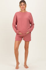 woman wearing a rose pink maternity sweatshirt and matching shorts, holding her baby bump