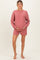 woman wearing a rose pink maternity sweatshirt and matching shorts, holding her baby bump