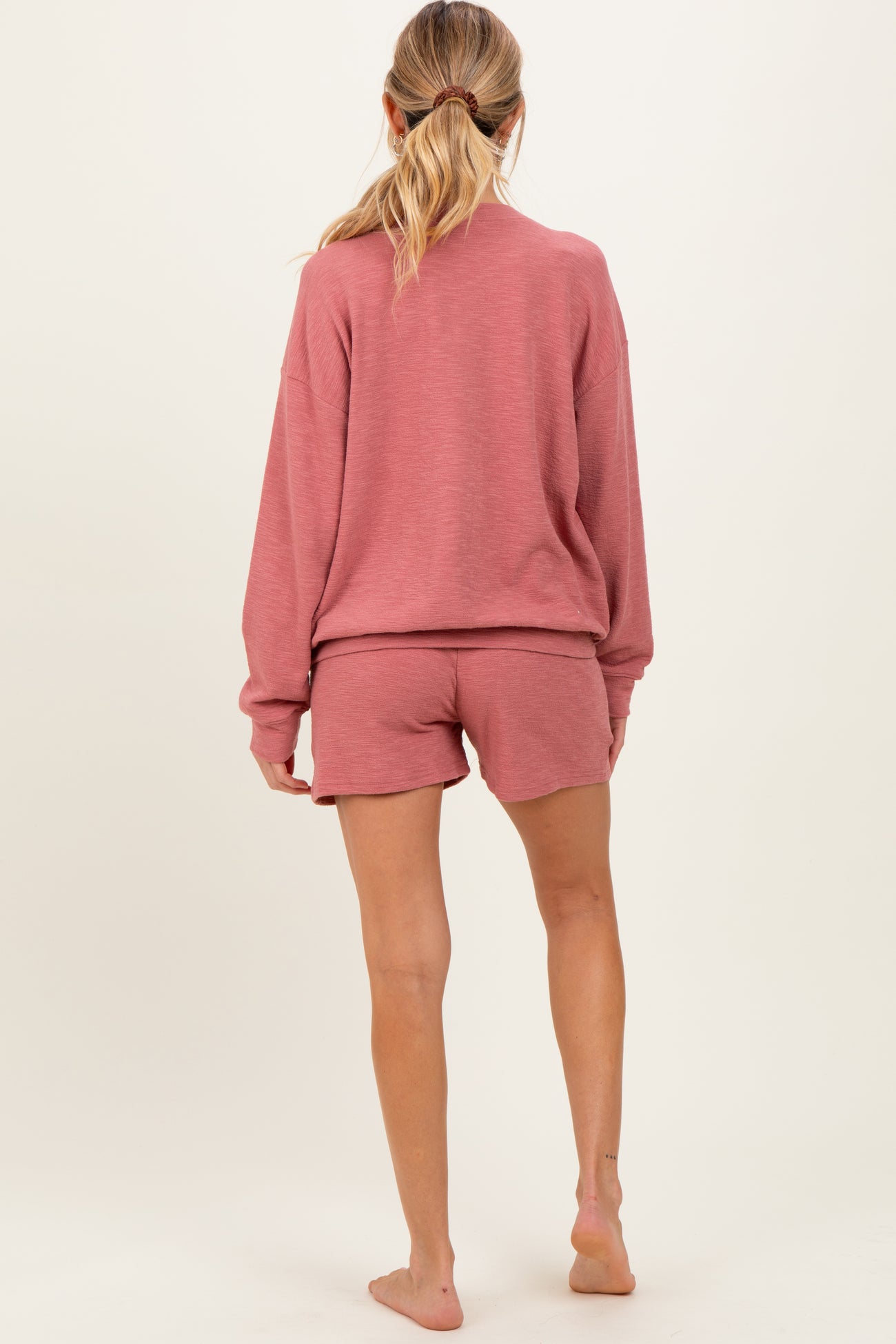 woman wearing a rose pink loose-fit maternity sweatshirt and matching shorts, showing her back