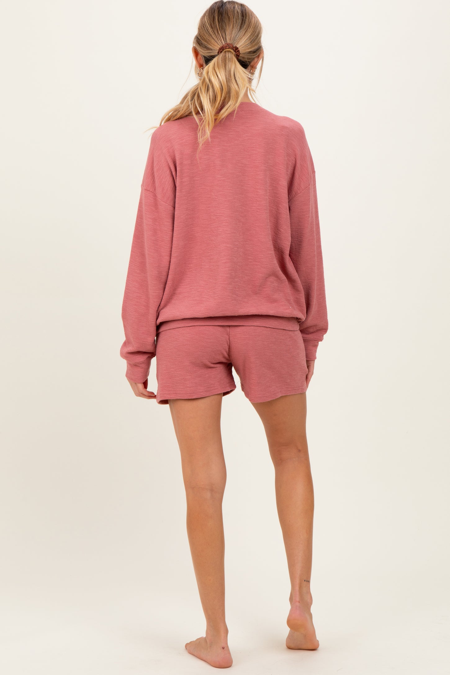 woman wearing a rose pink loose-fit maternity sweatshirt and matching shorts, showing her back