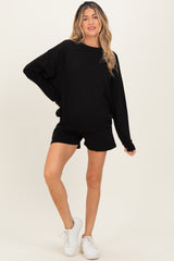 woman wearing a black oversized maternity sweatshirt and black shorts, showing her baby bump, paired with white sneakers