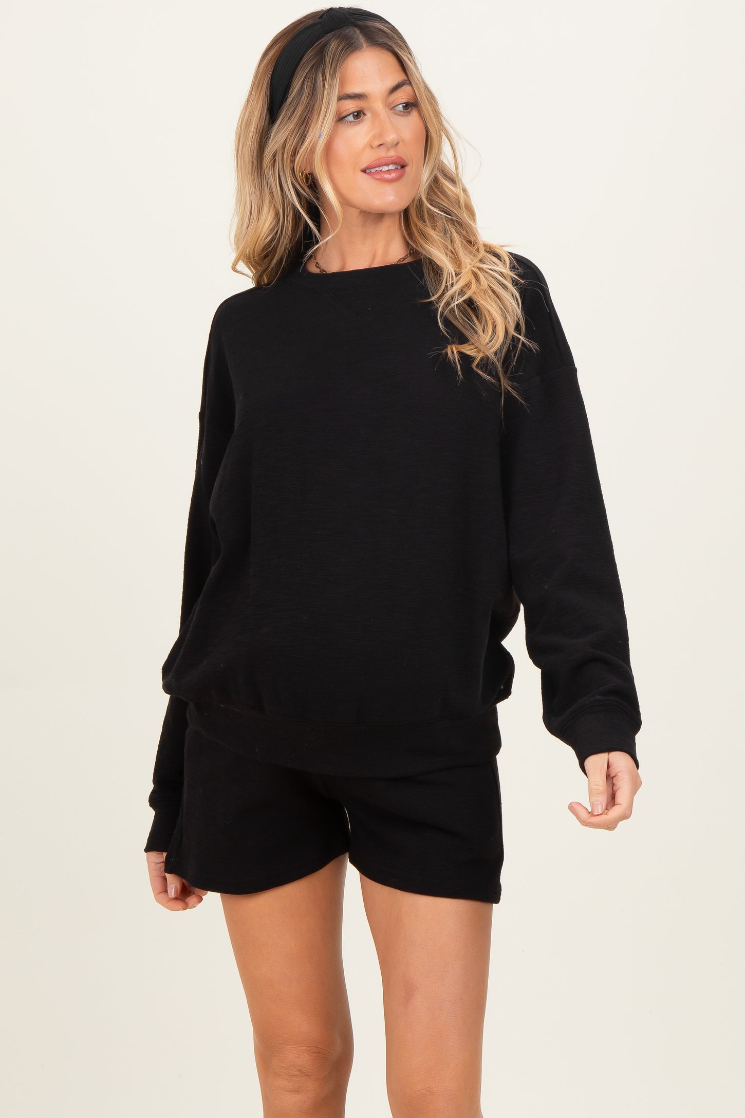woman wearing a black oversized maternity sweatshirt and matching shorts, styled with a headband