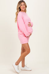 woman wearing a pink long sleeve maternity top and matching shorts, holding her baby bump