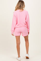 woman wearing a pink maternity sweatshirt and matching shorts, showing a casual back view