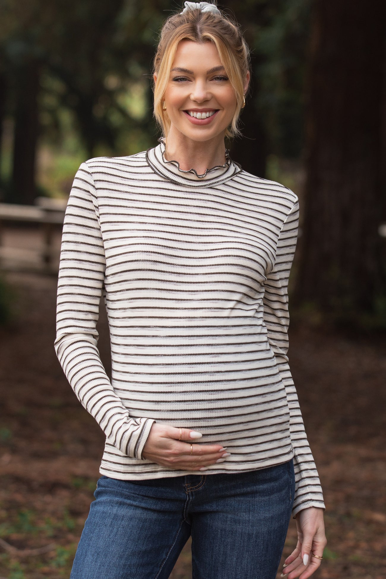 woman wearing a striped long sleeve maternity top and holding her baby bump