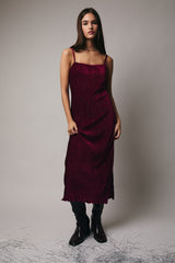 woman wearing a burgundy sleeveless midi dress with a textured finish and styled with knee-high black boots