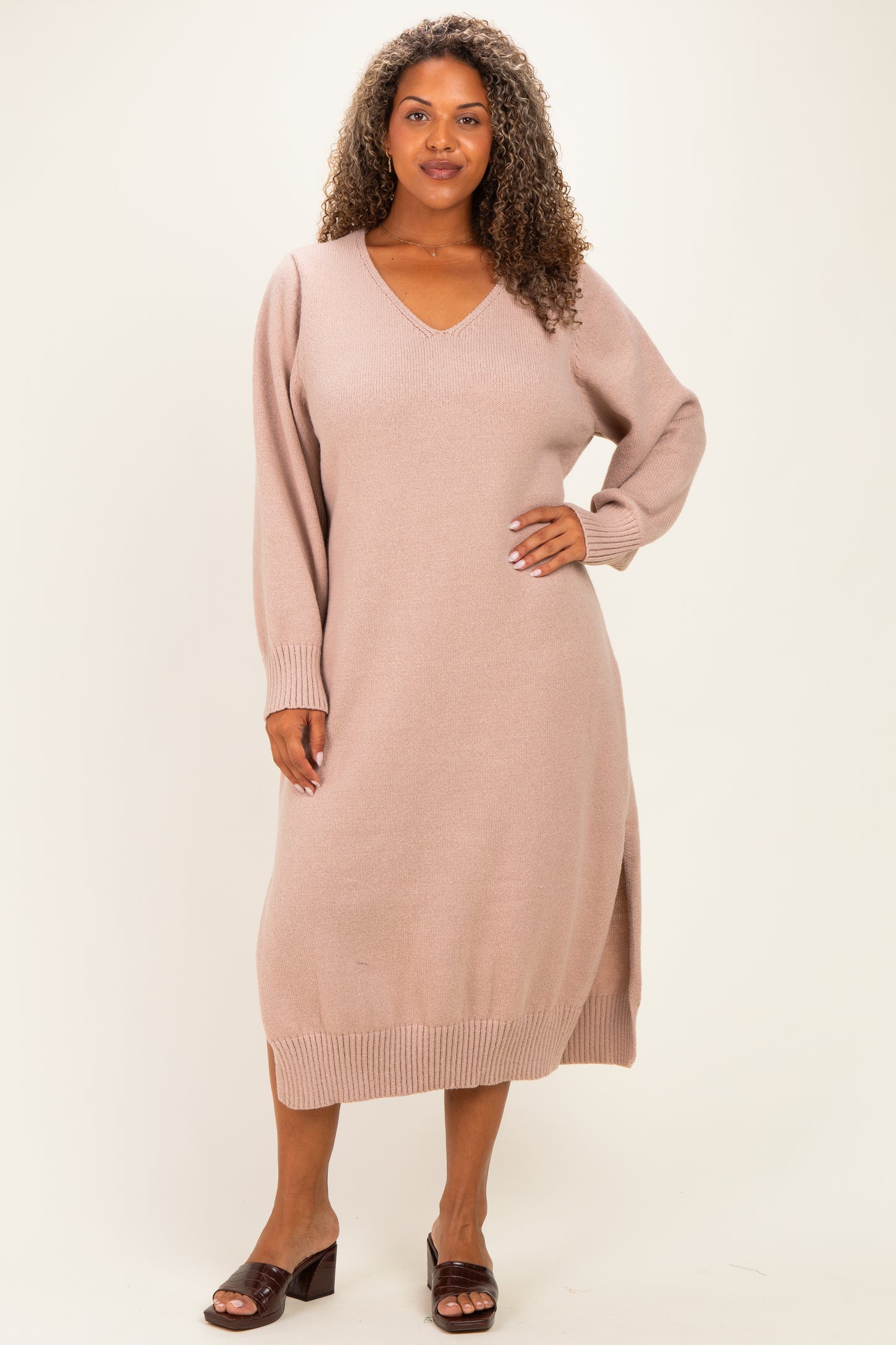 woman wearing a light pink long sleeve plus-size sweater dress with a v-neck and side slits
