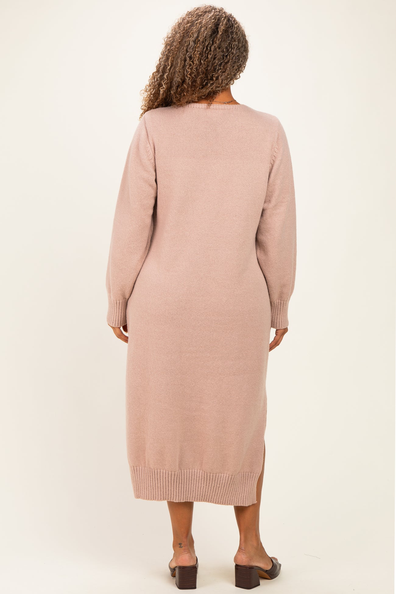 woman wearing a light pink long sleeve sweater dress with a slit at the hem and back detailing