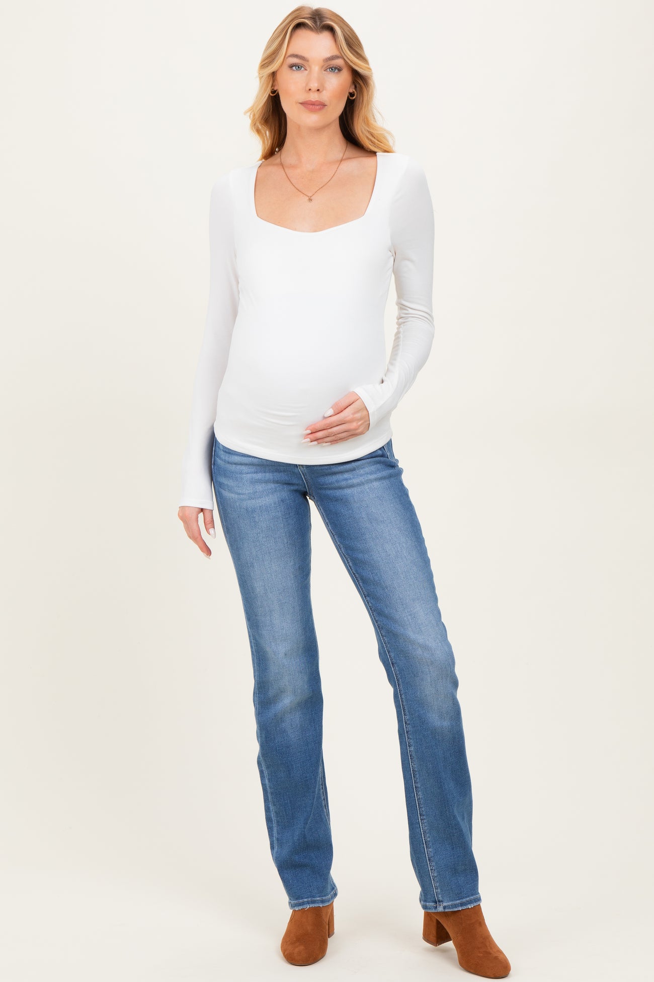 woman wearing a white long sleeve maternity top and blue jeans, displaying her baby bump