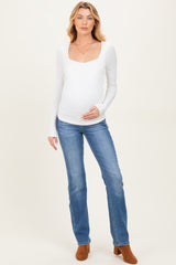 woman wearing a white long sleeve maternity top and blue jeans, displaying her baby bump