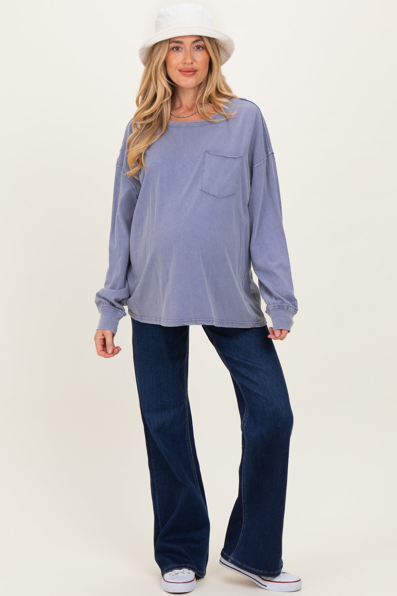 woman wearing a lavender oversized maternity top with a pocket and blue flared maternity jeans, showing her baby bump