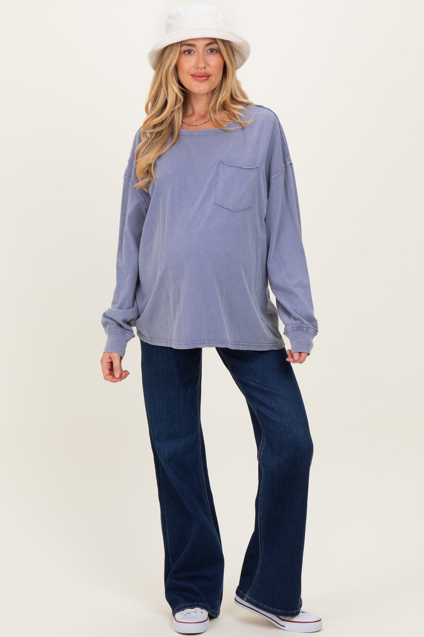 woman wearing a lavender oversized maternity top with a pocket and blue flared maternity jeans, showing her baby bump
